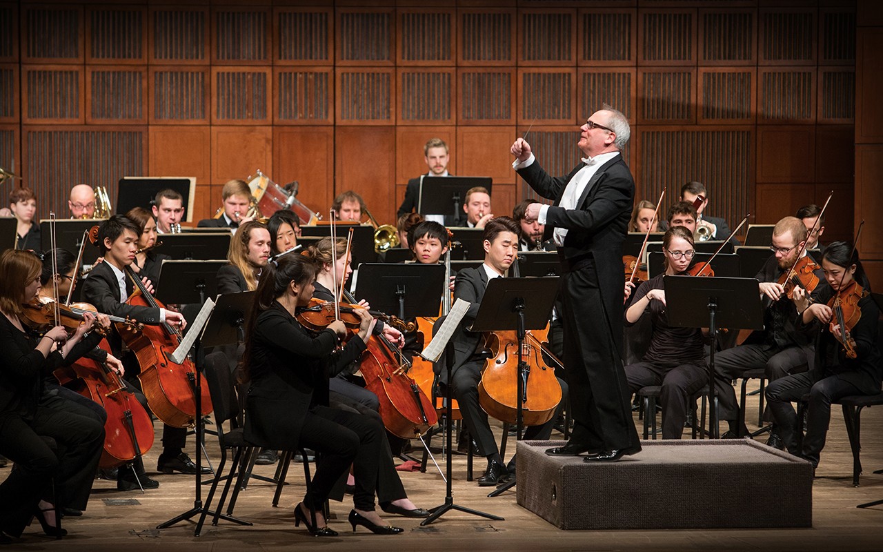 The philharmonia orchestra performs on stage while being conducted by maestro Mark Gibson.
