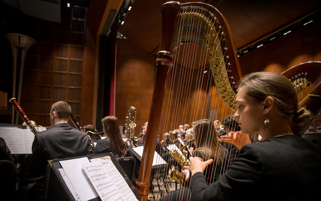 A female harp student performs with the Wind Symphony on the Corbett Auditorium stage