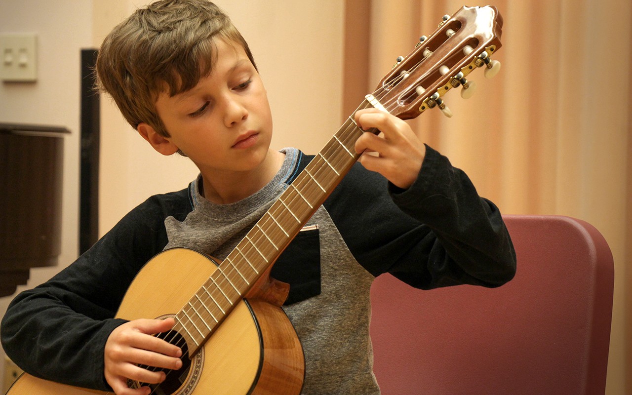 Middle school aged boy practices guitar during a lesson